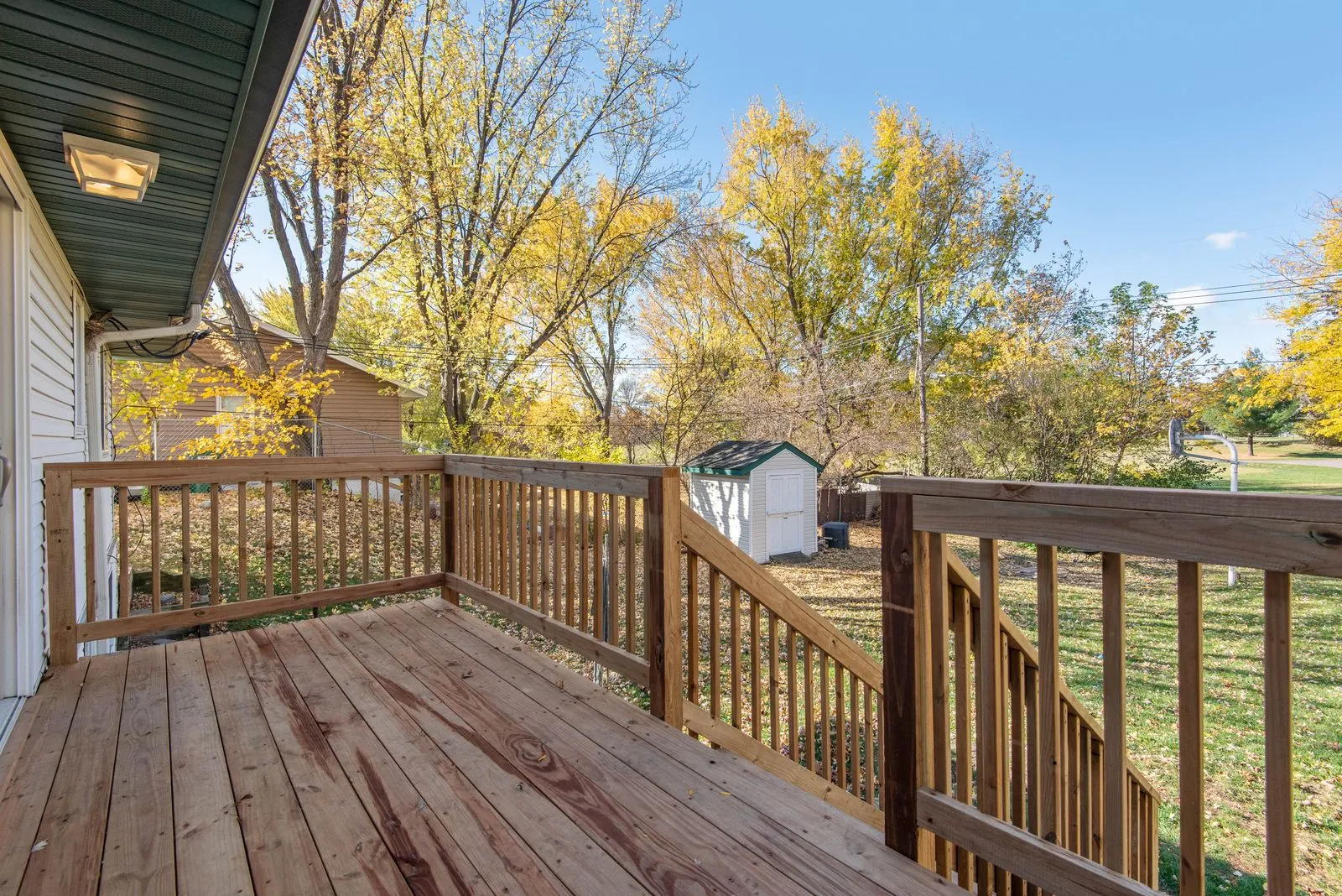 A wooden backyard deck with railings on a clear fall day
