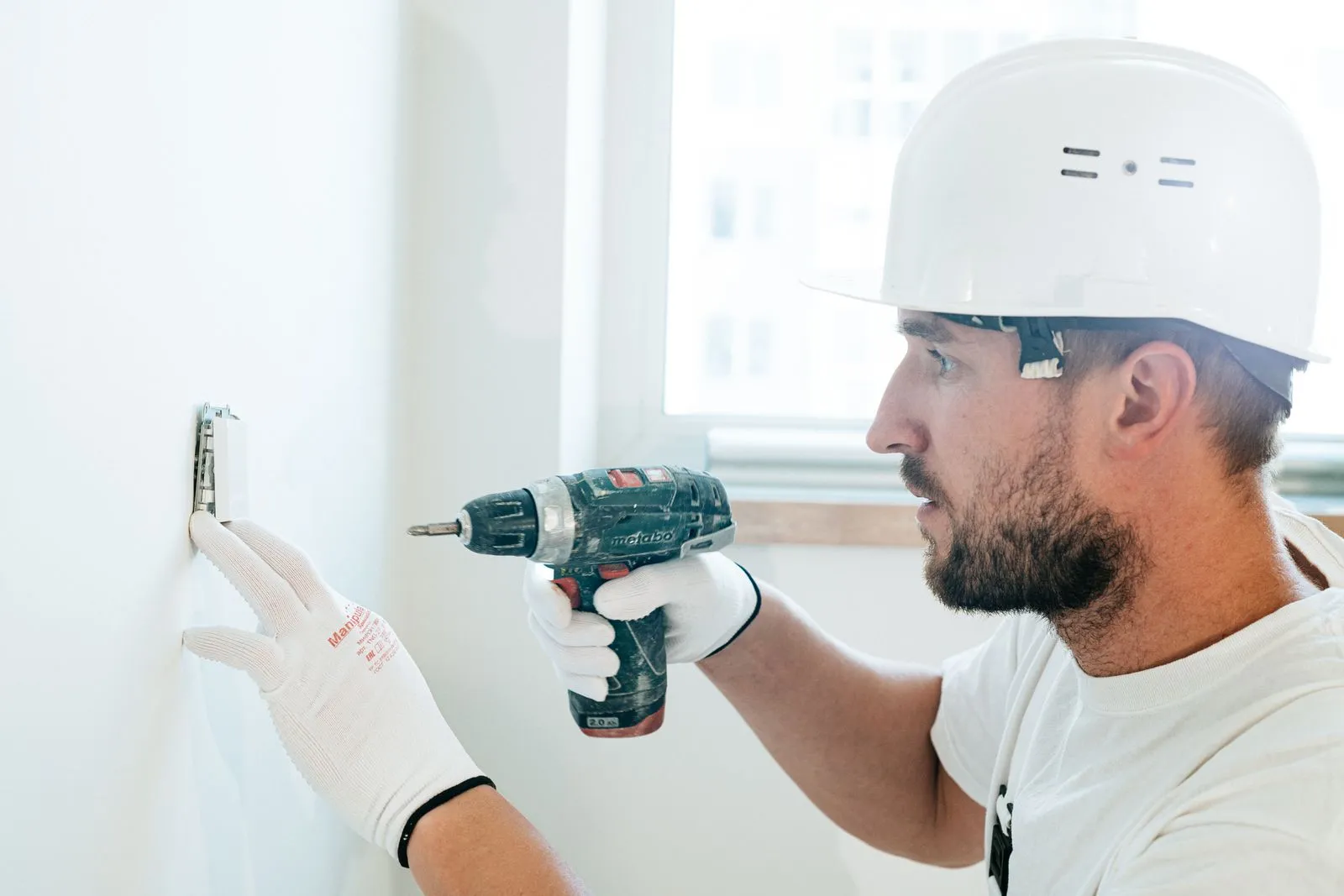 A handyman in safety gear drilling into an interior wall